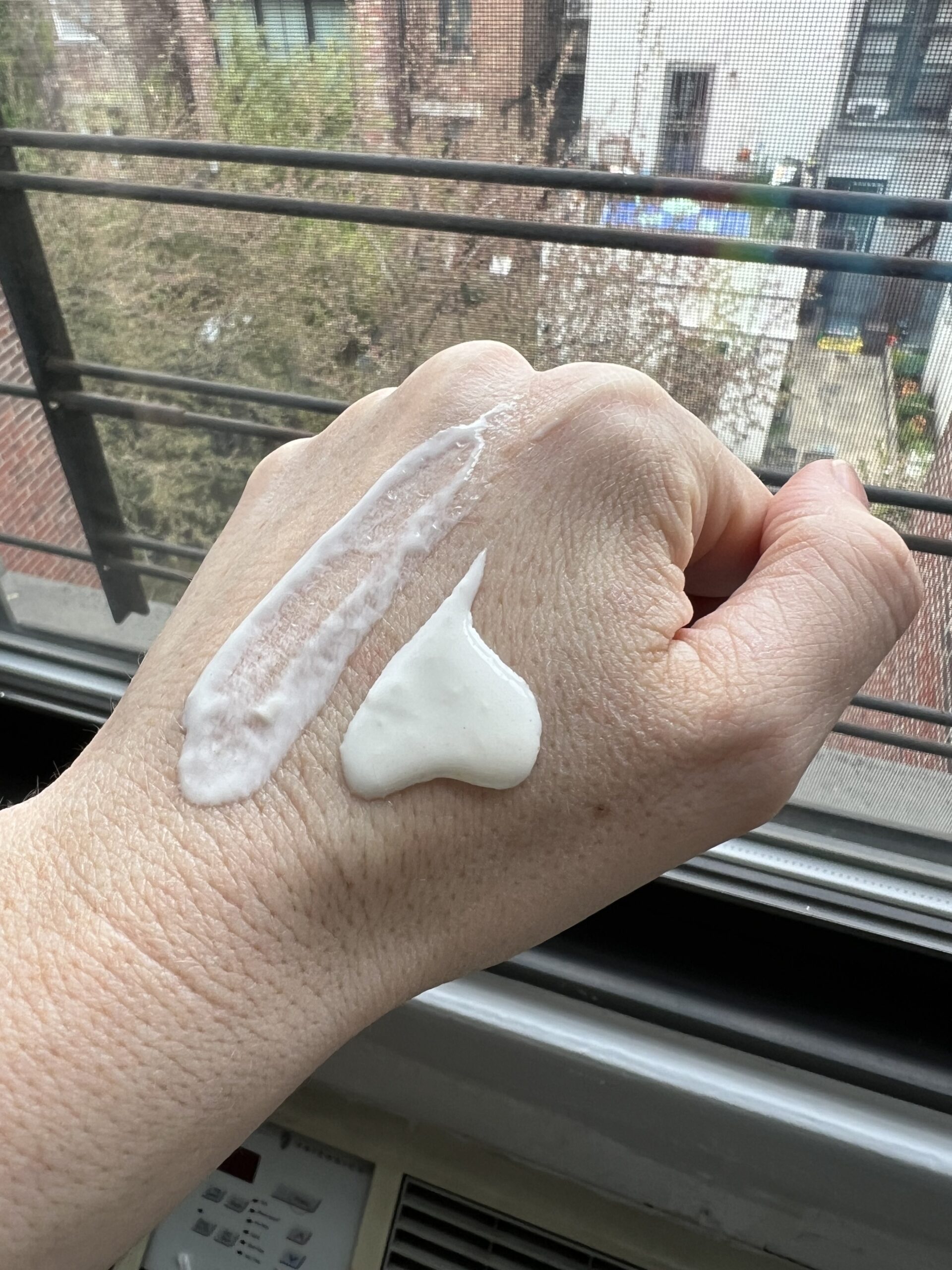 A hand with cream on it held up against a window
