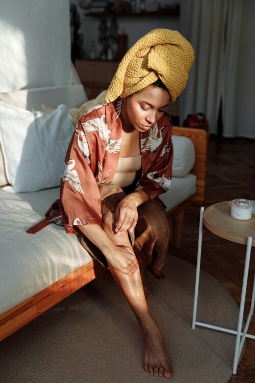 lotion after shaving Person with their hair wrapped in a yellow towel applies lotion to their legs