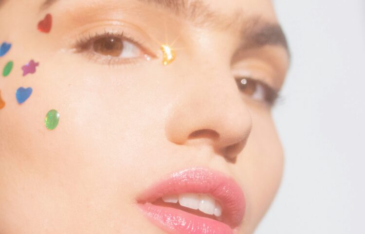Close-up of a person wearing colorful gems on their face to cover pimples without makeup