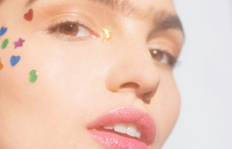 Close-up of a person wearing colorful gems on their face to cover pimples without makeup
